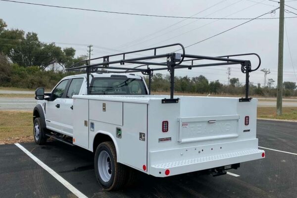 A white truck with tool compartments and a ladder rack facing left