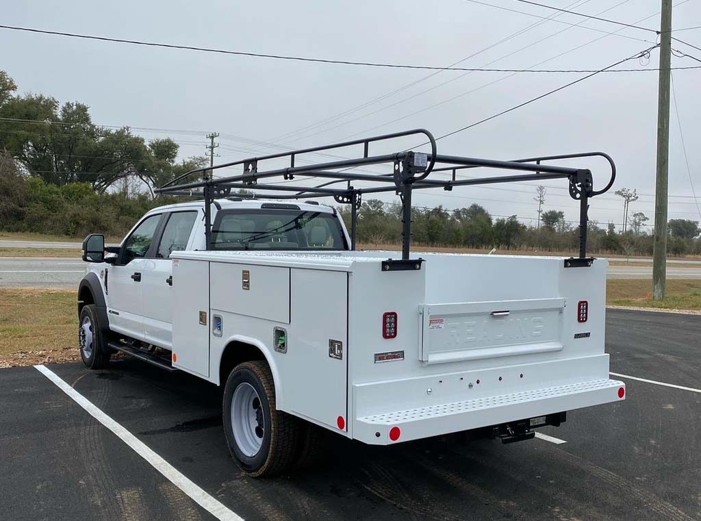 A white truck with tool compartments and a ladder rack facing left