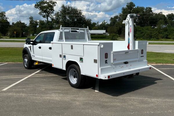 A white truck with tool compartments and a crane arm facing right
