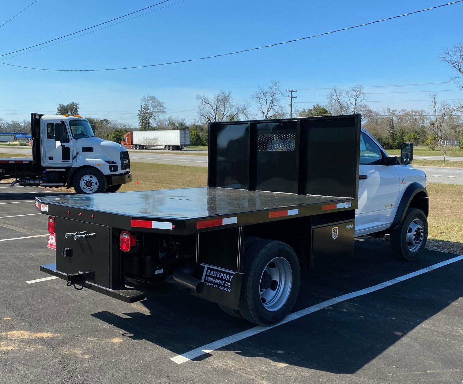 A white truck with a flatbed as seen from right rear