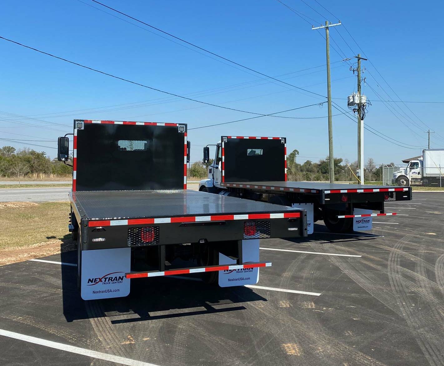 Two black trucks with a flatbeds as seen from left rear