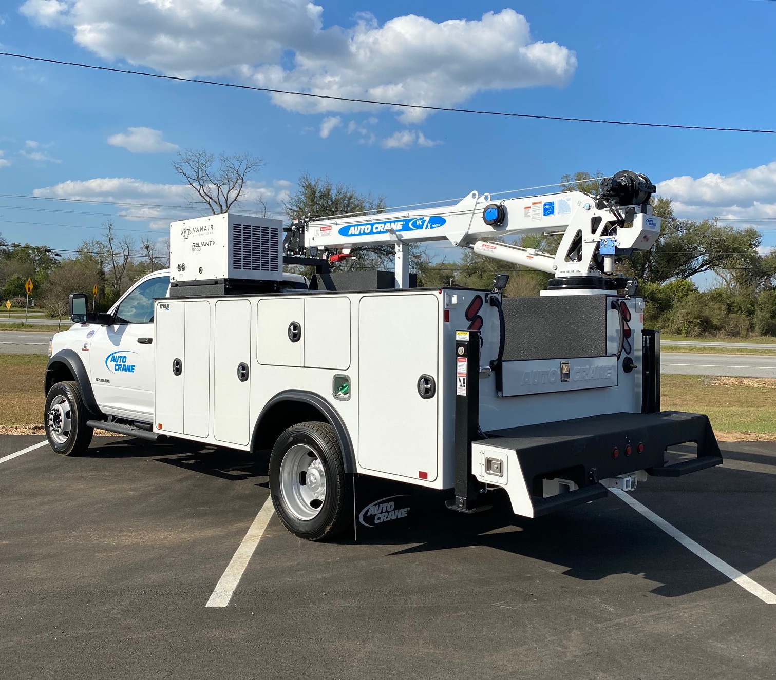 A large white truck with tool compartments and a crane arm viewed from left rear